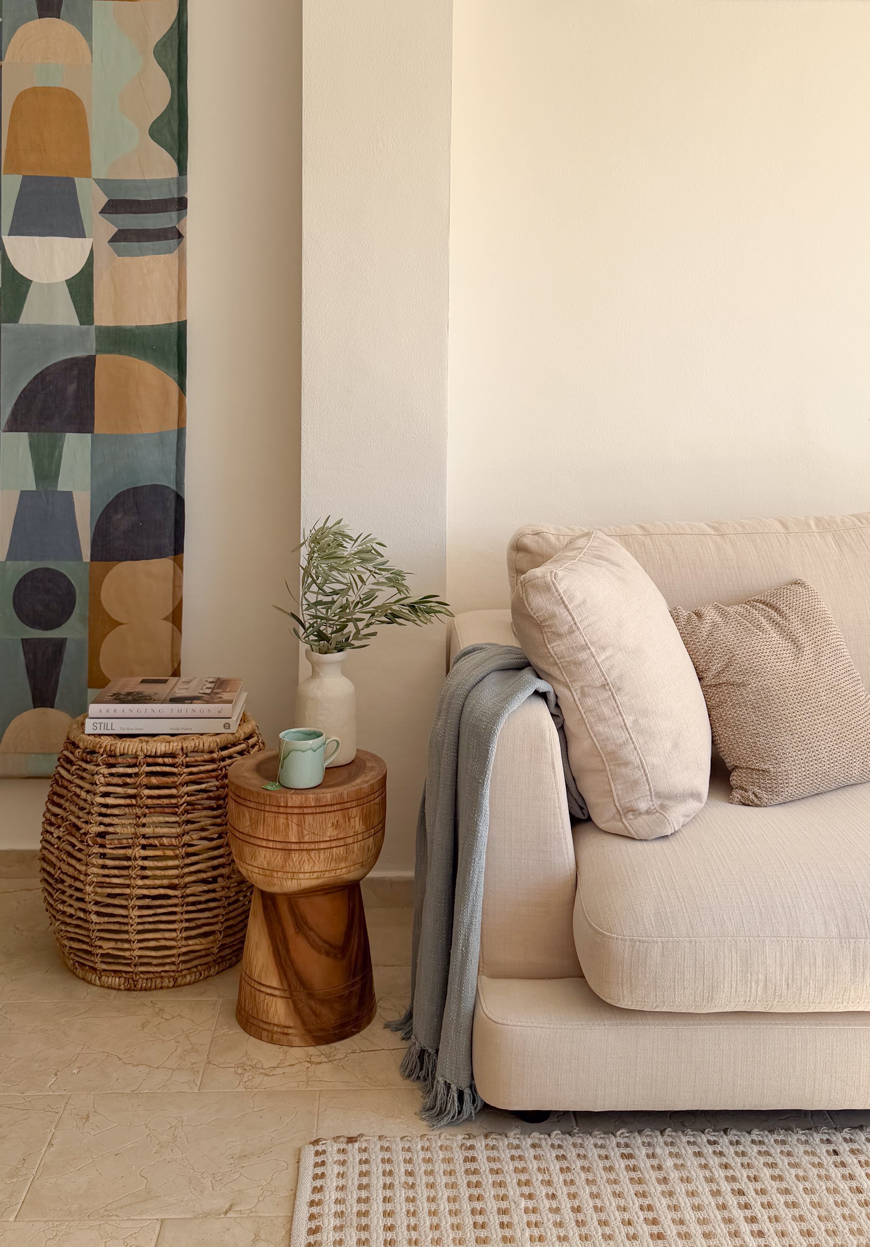 Living room corner with a woven basket, wood side table, and a colorful geometric tapestry on the wall
