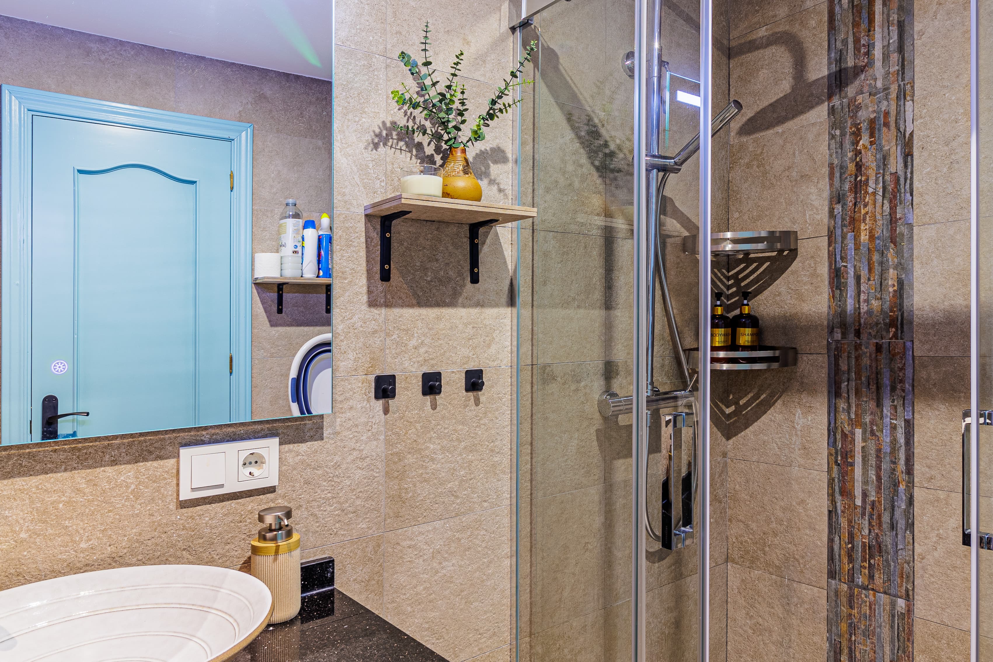 Bathroom mirror reflecting a pale blue door, with an oval sink and black stone counter in the foreground