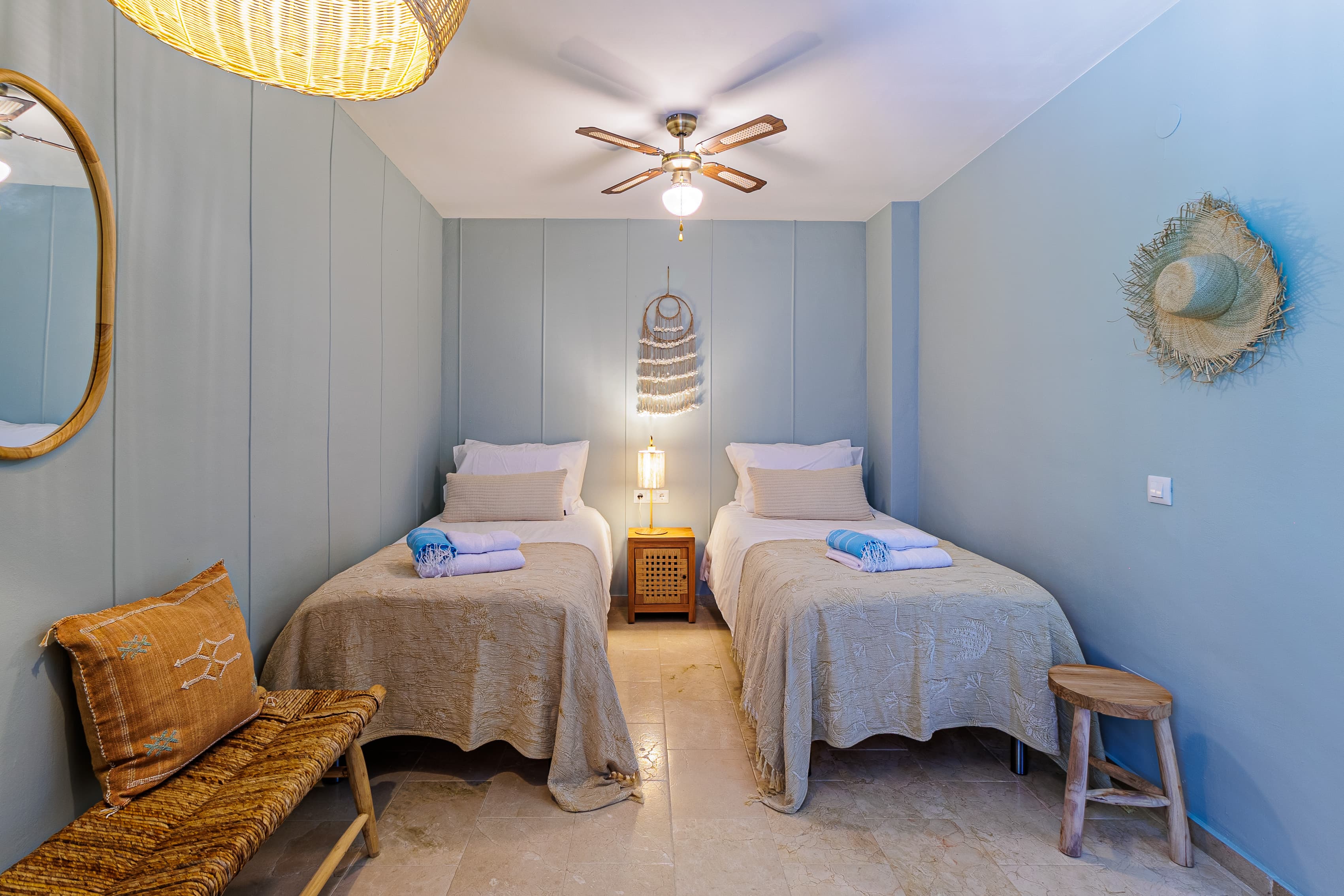 Twin bedroom bed with a straw hat on the wall, and a light-blue door open to the hallway beyond