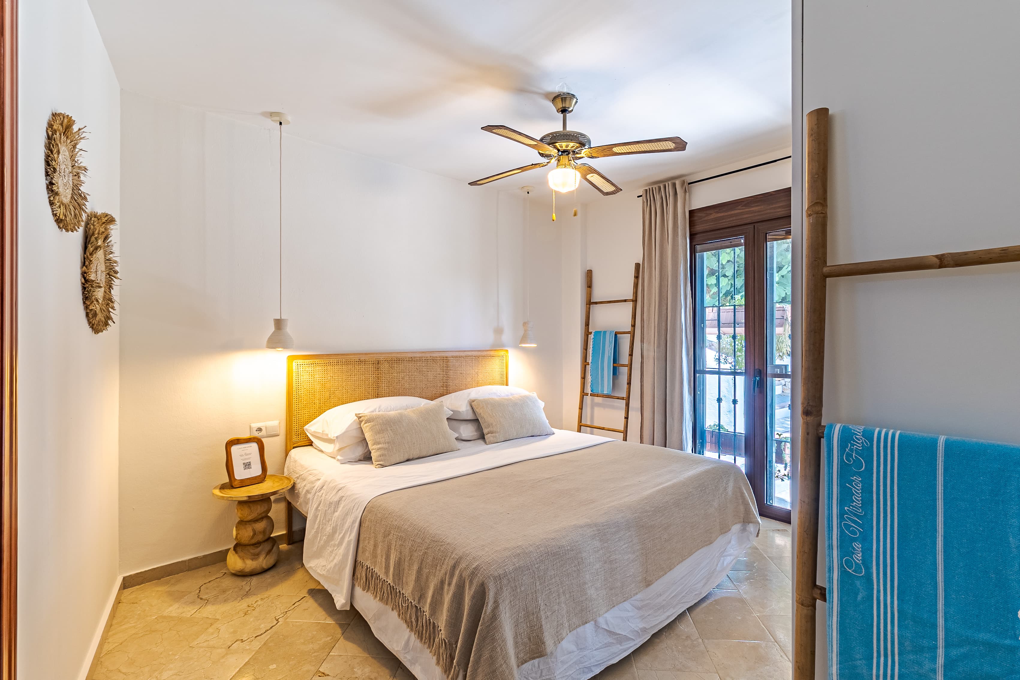 Master bedroom with a rattan cane headboard, linen bedspread, and glass doors open to a private terrace