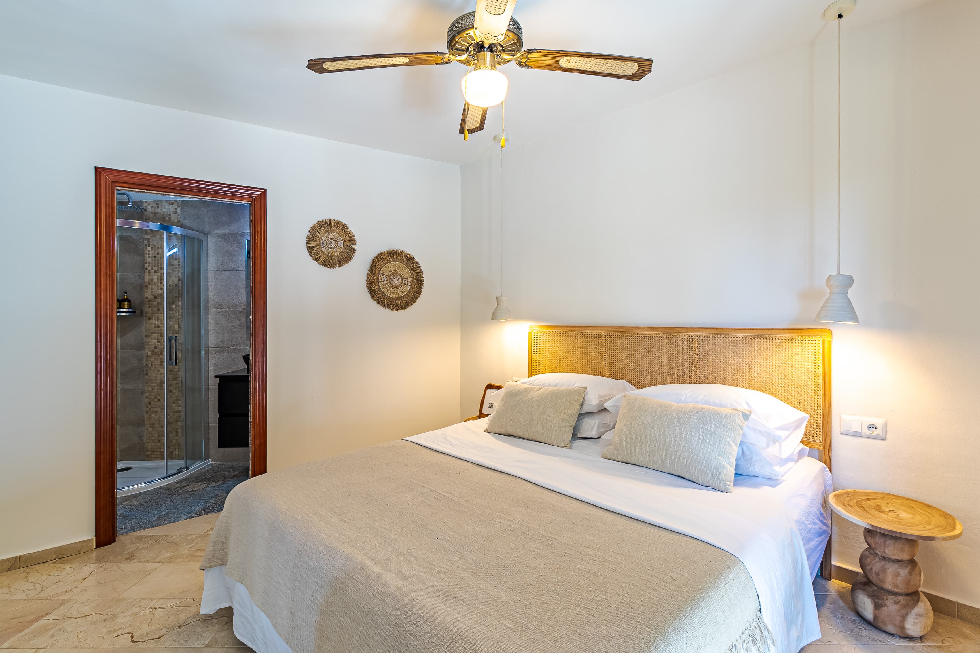 Master bedroom bed with a cane headboard, straw wall discs, and a doorway open to the ensuite shower