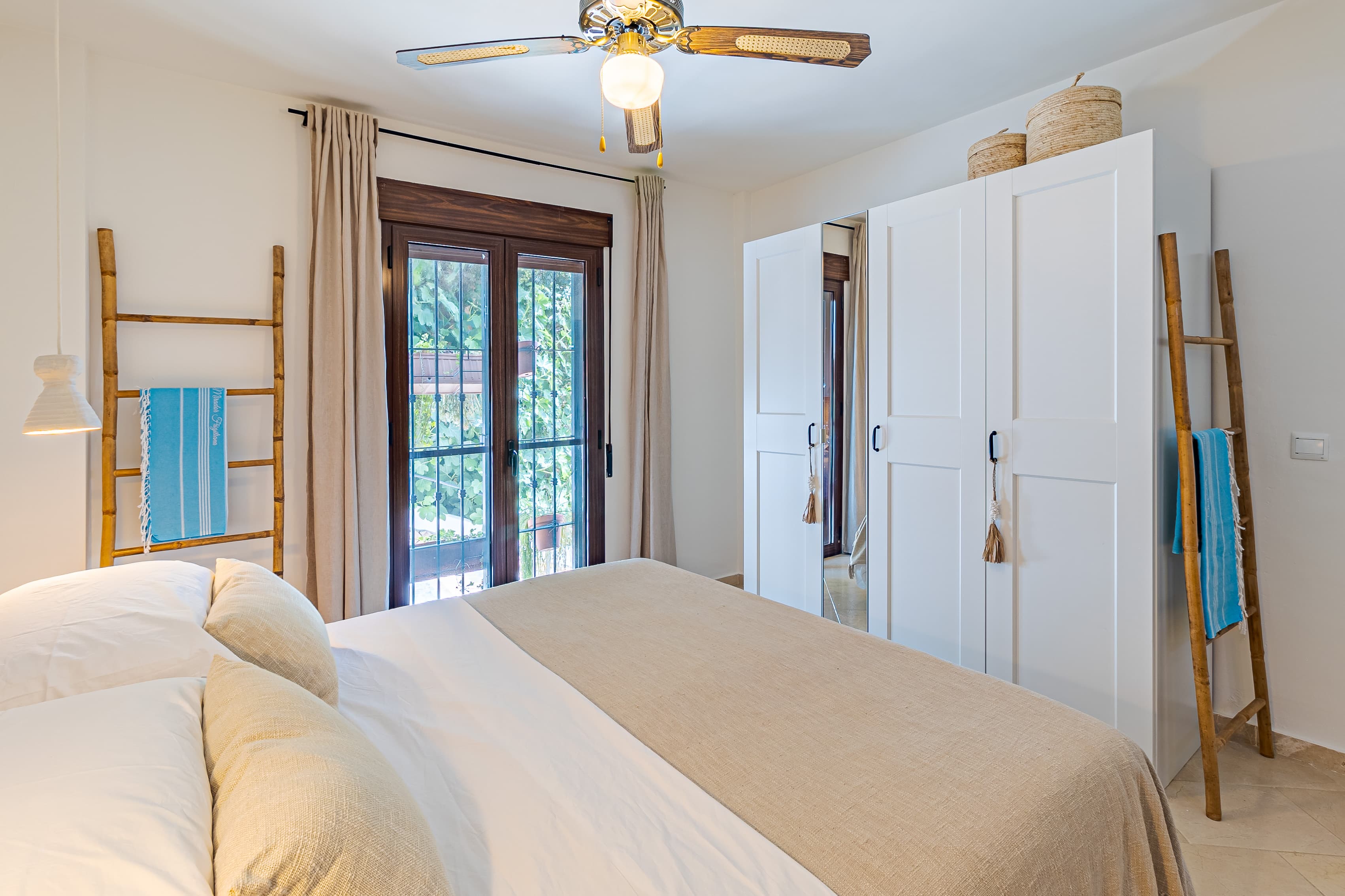 Bed foreground with a mirrored wardrobe and bamboo towel ladder against the window