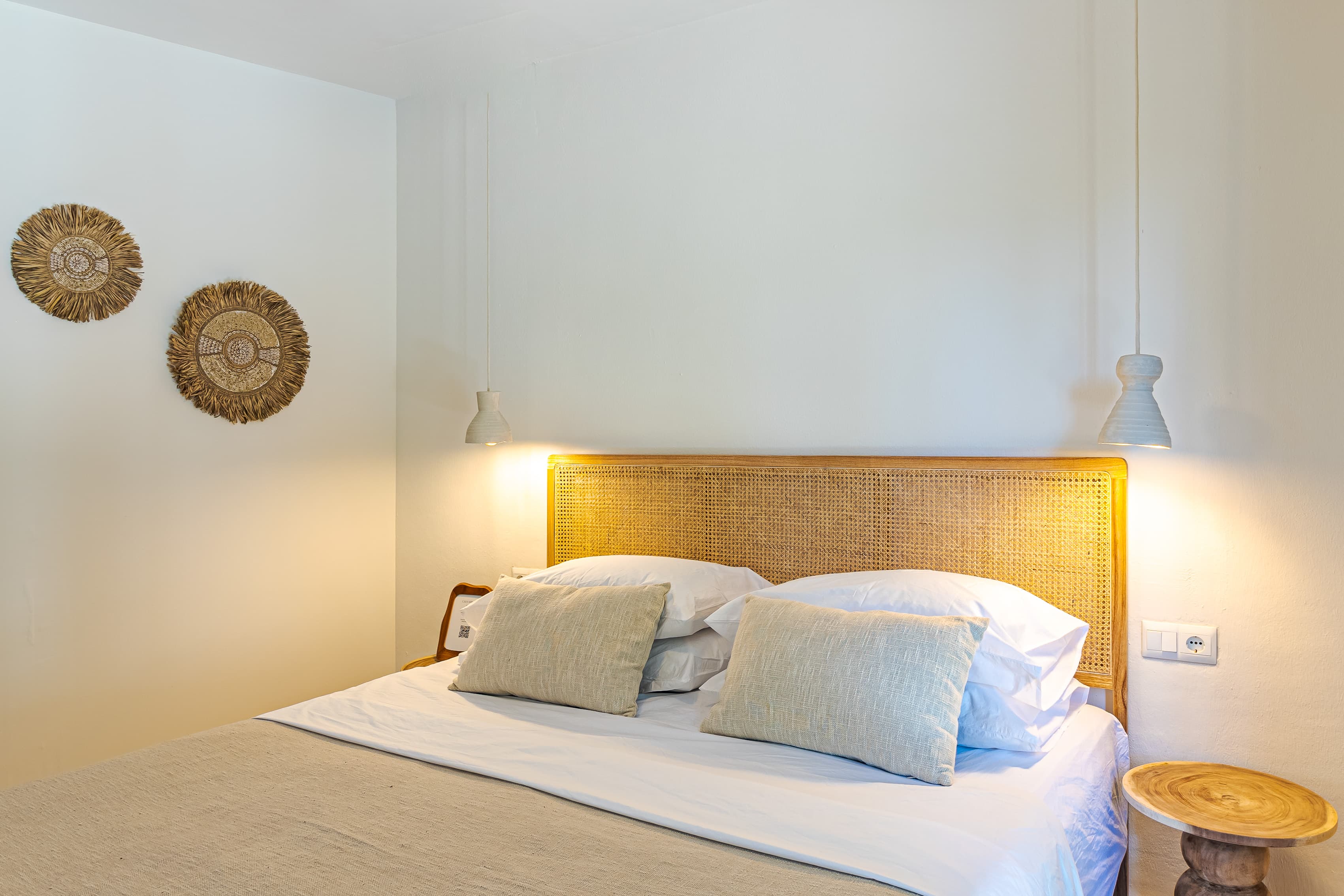 Cane headboard bed flanked by pendant lights, with woven straw wall discs above a wooden side table