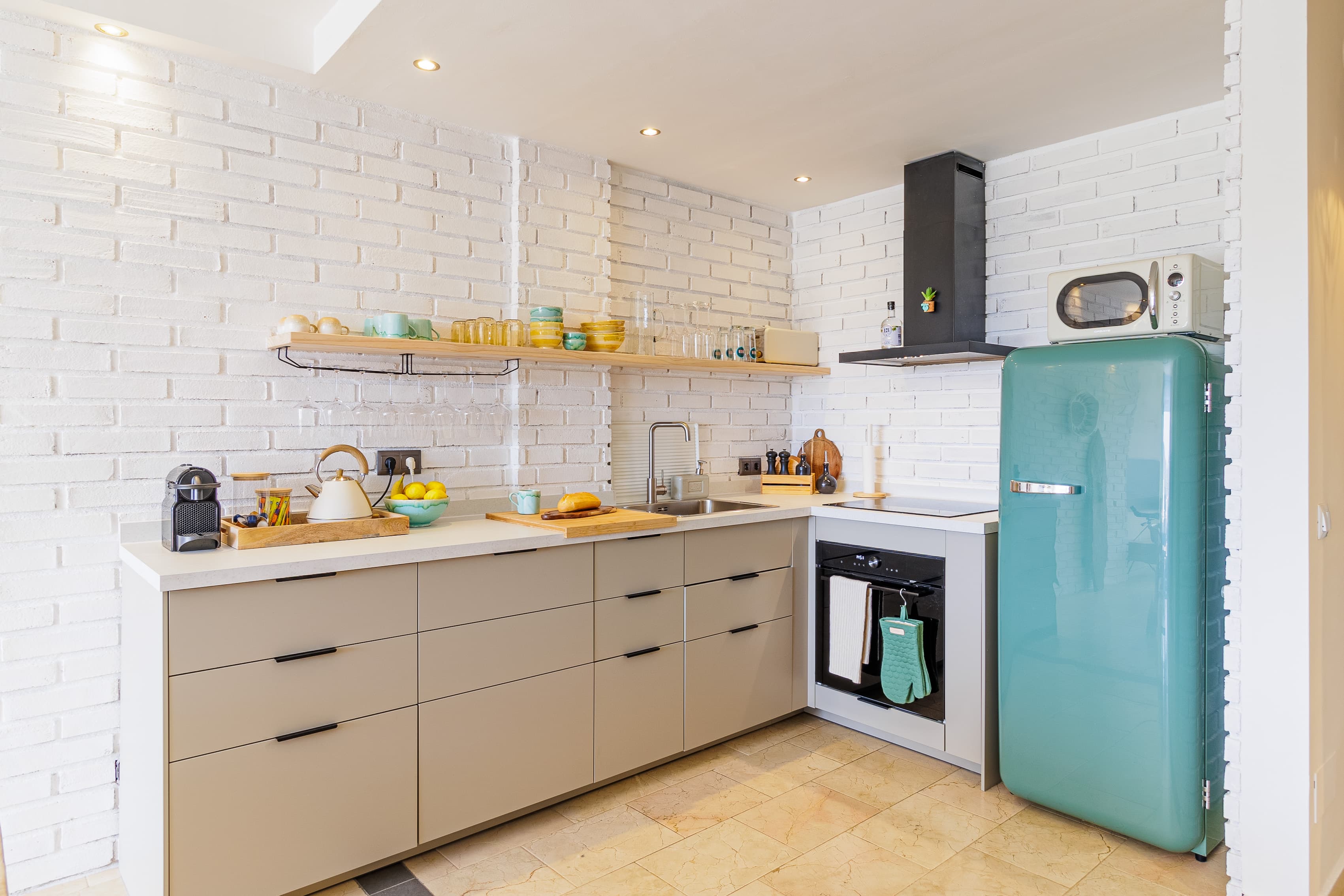 Kitchen view of the whitewashed brick wall and open shelving, with a woman by the mint-green fridge