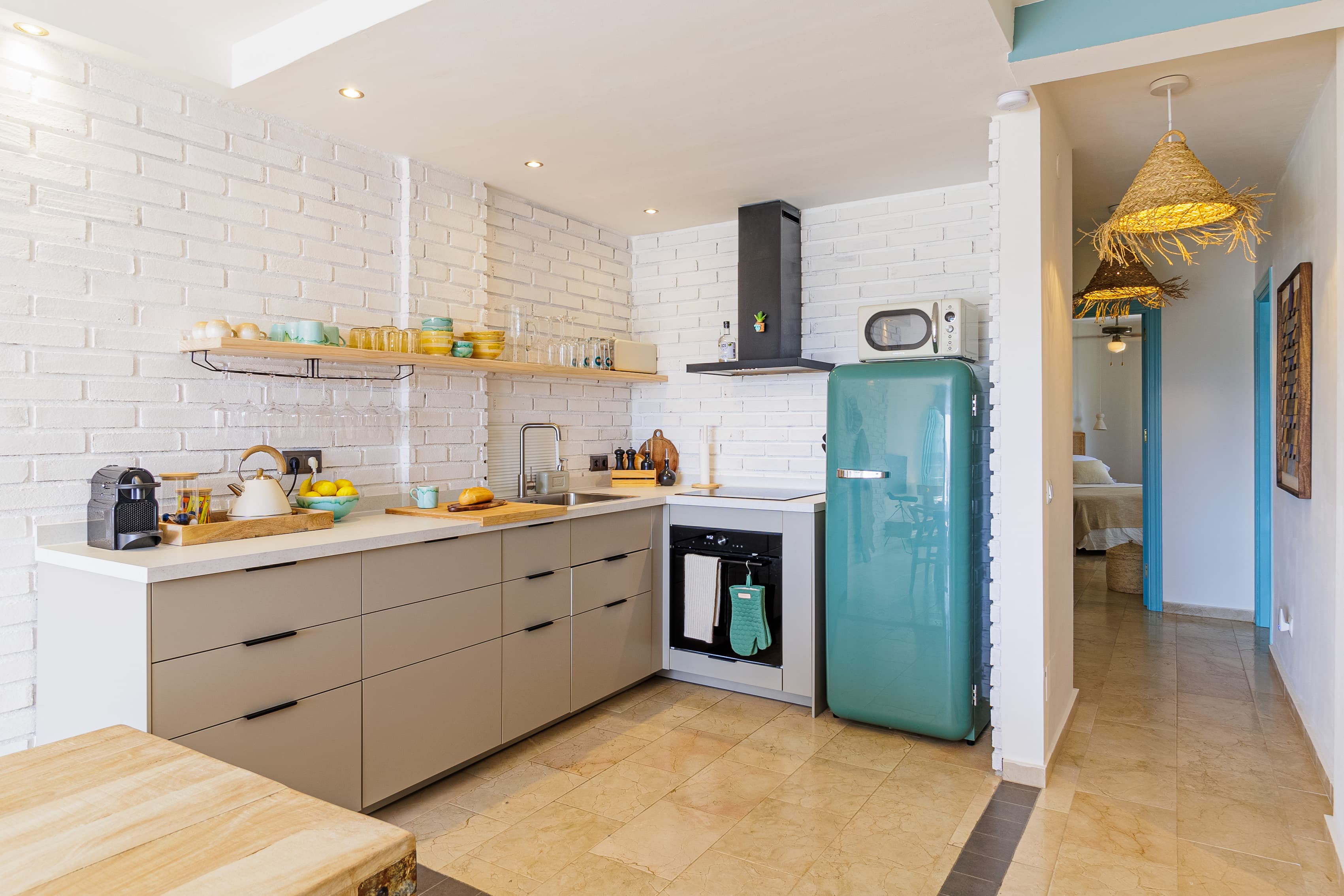 Wide view of the kitchen's white brick walls, open shelving, and mint-green retro fridge beside the hallway