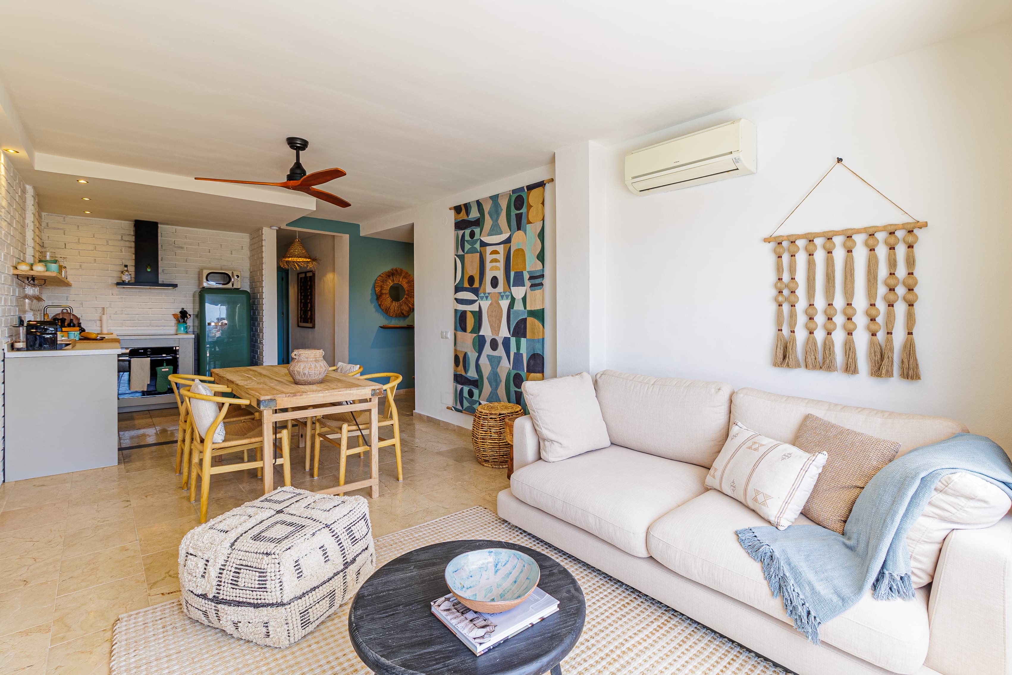 Living area with a cream sofa, woven wall hanging, and a round black coffee table holding a ceramic bowl and books