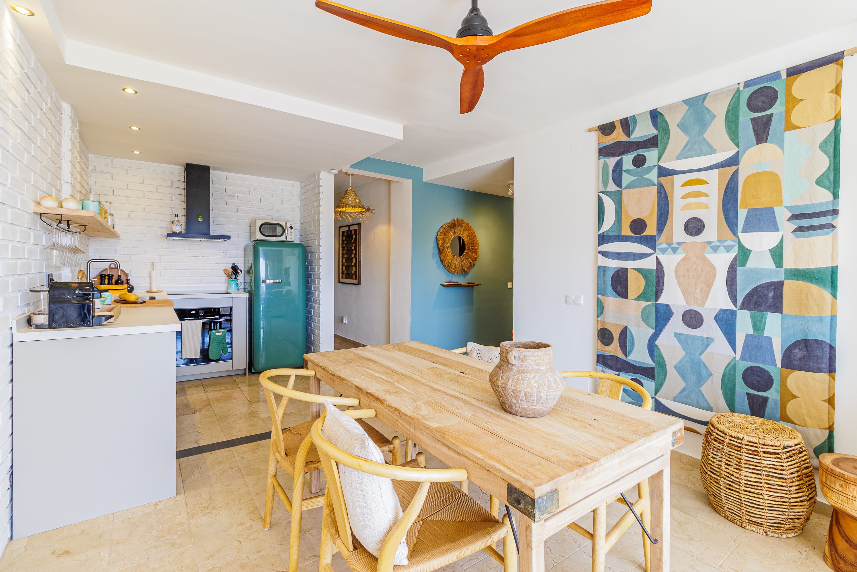 Dining table with a terracotta pot, a mint-green retro fridge, and a geometric wall tapestry