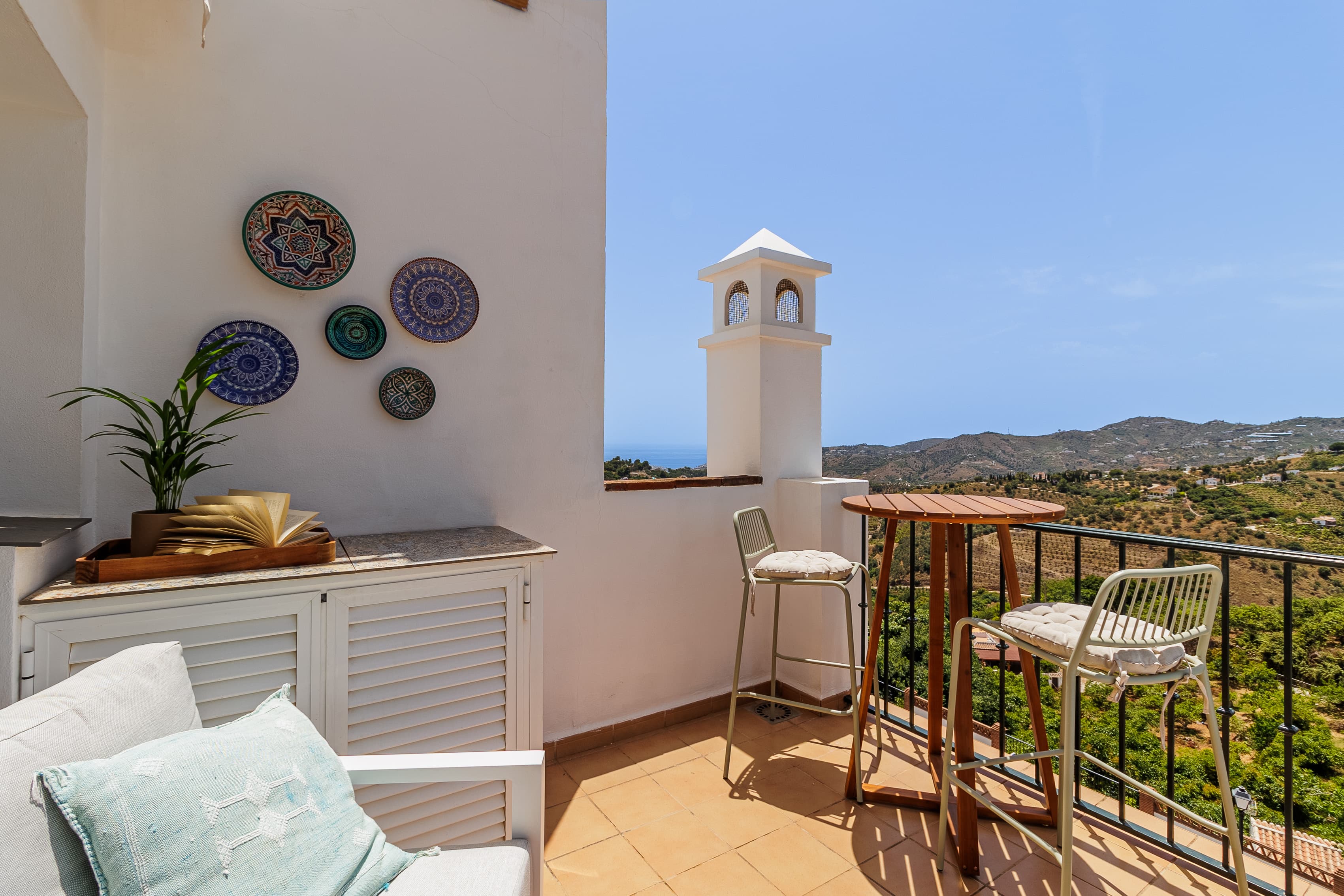 Terrace lounge with a blue throw and straw hat on the sofa, overlooking the whitewashed hillside village