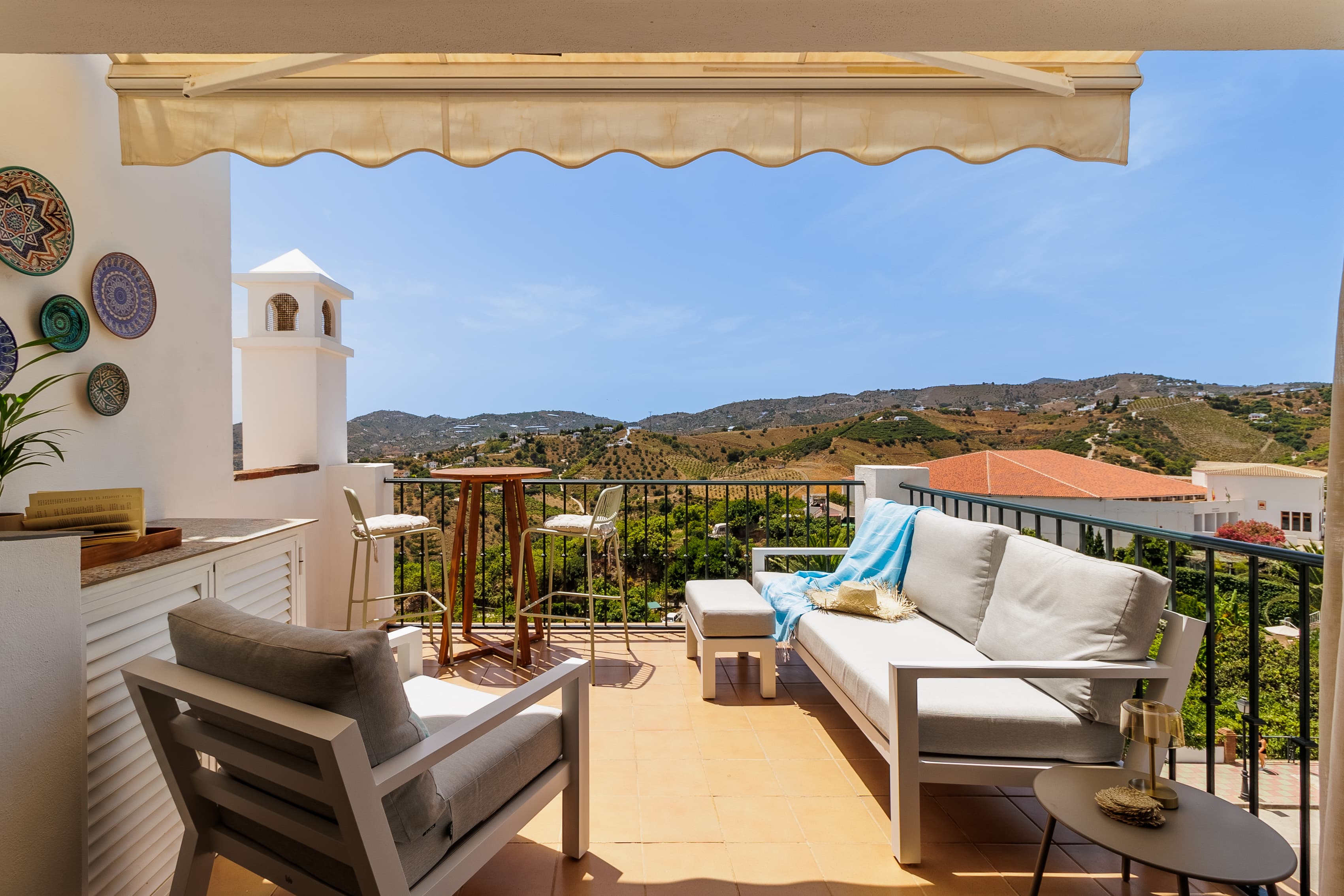 Covered terrace lounge with sofas beneath an awning, mountain views beyond